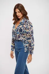 Camisa de manga larga con cuello clásico y cierre frontal de botones. Presenta un estampado abstracto en tonos azules, beige y marrón oscuro, con un corte holgado y fluido.