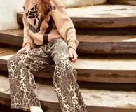 Pantalón de jean con estampado animal print en tonos beige y negro, de corte ancho y tiro medio. Presenta detalles de cuero bordó en la pretina y los bolsillos.