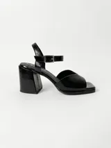 Sandalia de cuero negro con acabado charol, diseño de punta cuadrada, taco bloque forrado y tira con hebilla metálica ajustable en el tobillo.