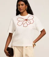 Blusa boxy Marfinno de mangas cortas y cuello redondo, confeccionada en algodón blanco, con diseño holgado y bordado floral en relieve de color marrón en el frente.