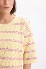 Sweater de punto fantasía color amarillo con líneas horizontales onduladas en color fucsia, de cuello redondo y manga corta.