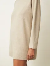 Vestido corto de color beige con cuello alto y mangas largas, de corte recto y holgado.