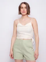 Top de tejido acanalado color beige claro, con escote drapeado tipo cowl neck y tirantes finos. Presenta un frunce ajustable con cordón en el lateral izquierdo que crea un efecto drapeado.