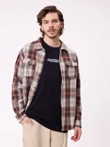 Camisa de franela gruesa con diseño a cuadros en tonos marrones, beige y azul. Presenta cuello clásico, cierre frontal con botones y dos bolsillos en el pecho con solapa y botón.