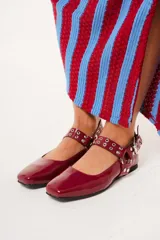 Balerinas color borgoña de charol con punta cuadrada, correa con hebilla y apliques metálicos.