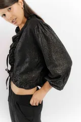 Blusa negra de lino con acabado brillante, de manga larga abullonada, escote con volados y cierre frontal con tiras para anudar.