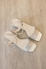 Sandalias de fiesta con diseño elegante y minimalista, confeccionadas en cuero con acabado metalizado plateado. Presentan una tira ancha sobre el empeine, puntera cuadrada, correa fina con hebilla ajustable al tobillo y tacón ancho de altura media.
