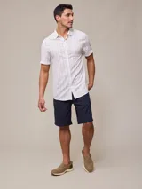 Camisa de manga corta para hombre, color blanco con rayas verticales finas en relieve. Tiene cuello abotonado, bolsillo en el pecho izquierdo y logo bordado pequeño.