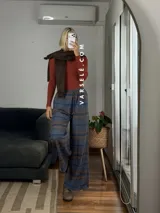 Pantalón tipo palazo de corte amplio y tiro alto, confeccionado en tela con estampado de cuadros escoceses en tonos marrones, blancos y negros. Cuenta con cintura elástica y bolsillos laterales.