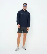 Chaqueta deportiva masculina de color azul marino, confeccionada en tejido técnico repelente al agua con acabado texturizado. Presenta cierre frontal con cremallera, capucha integrada y estampado de coordenadas en el pecho.