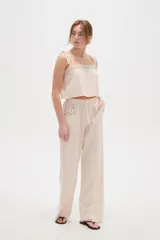 Pantalón ancho de viscosa color beige claro, de tiro alto con cintura elastizada y cordón ajustable. Presenta bolsillos laterales decorados con detalles bordados geométricos.