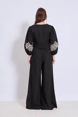 Blusa negra con cuello redondo y mangas largas abullonadas, con apliques bordados de hojas en color crudo en el frente y en las mangas.