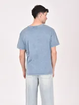 Remera color beige con estampa rectangular con diseño abstracto en tonos marrones y texto.