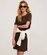 Vestido corto marrón oscuro, estilo camiseta, con escote redondo, mangas cortas y bolsillos laterales. El bajo es redondeado.
