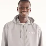 Campera New Balance de hombre, modelo Trackside, de color gris. Presenta capucha con cordón ajustable, cierre frontal completo y el logo de la marca estampado en el pecho.