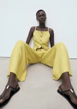 Pantalón de tiro alto color amarillo con sutil diseño de rayas verticales, de corte recto y largo, con bolsillos laterales y cierre frontal de botón y cremallera.
