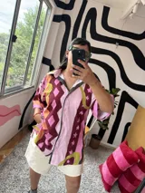 Camisa de manga corta con cuello, diseño estampado abstracto y geométrico en tonos rosados, marrones, amarillos y verdes. Cierre frontal.