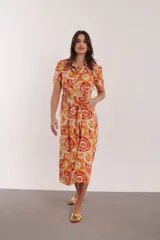Vestido midi con estampado de círculos concéntricos en tonos naranja, amarillo y blanco. Tiene cuello camisero, mangas cortas y cinturón de la misma tela.