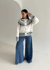 Cardigan de punto con diseño jacquard de inspiración nórdica, en tonos blanco, gris y marrón. Presenta cuello redondo, cierre frontal con botones y mangas largas con puños acanalados.