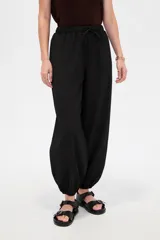 Pantalón babucha negro de tiro medio con cintura elástica y cordón ajustable, corte holgado y botamangas con elástico fruncido.