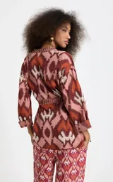 Kimono de punto Le Lis Blanc modelo Bina, con patrón jacquard geométrico en tonos rosados, marrones y crudo. Presenta escote en V profundo con ribete acanalado, mangas anchas de largo medio, corte holgado y cinturón de la misma tela para atar en la cintura.