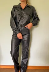 Mono largo negro de cuero sintético con textura de cocodrilo, cuello camisero, cierre frontal con botones, mangas largas con puños elásticos, bolsillos con solapa en el pecho y corte recto.