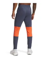 Pantalón deportivo Under Armour de la colección Challenger, color azul oscuro con detalles laterales en naranja. Presenta corte ajustado, cintura elástica con cordón, bolsillos laterales y cremalleras en los tobillos.
