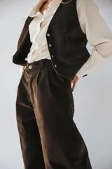 Pantalón de pana marrón, de corte holgado, con bolsillos laterales y traseros. Se ajusta a la cintura con cinturón de cuero marrón.