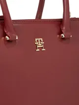 Cartera tote de Tommy Hilfiger color borgoña, con doble asa de mano y correa larga extraíble y ajustable. Tiene cierre magnético, dos compartimentos principales y tres bolsillos interiores con cremallera.