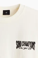 Remera de algodón en color blanco, de corte holgado, con cuello redondo acanalado, mangas cortas y hombros caídos. Presenta un pequeño estampado en el pecho con la inscripción "SOHO CHAMPIONS New York City".