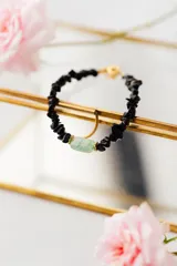 Pulsera elástica con cuentas de piedra negra irregulares y una cuenta central cilíndrica de color verde agua.