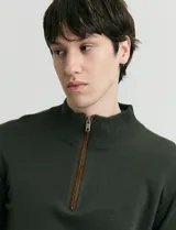 Sweater de punto color verde oliva, con cuello alto y medio cierre frontal. Presenta coderas en símil nappa y puños acanalados.