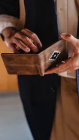 Billetera de cuero sintético color marrón con efecto desgastado, presenta un detalle bordado geométrico en el frente. Cuenta con doble compartimento para billetes, tarjeteros y visor interior.