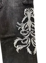 Jean de corte oxford y tiro bajo, color negro con efecto lavado. Presenta estampa bordada en la parte inferior de una de las piernas y detalles de costuras reforzadas en las rodillas.