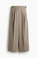 Pantalón sastrero de sarga color beige, de pernera ancha y tiro medio. Presenta pinzas frontales, raya marcada en las piernas y trabillas ajustables con botones en los laterales de la cintura.