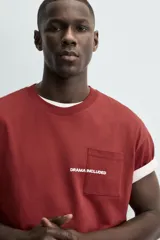 Camiseta blanca de corte relajado (relaxed fit) con cuello redondo y manga corta. Presenta un bolsillo plastrón en el pecho y un estampado de texto en color marrón rojizo en la espalda que dice "SOMETIMES SÍ, SOMETIMES BYE" (reemplazando la 'O' de 'SOMETIMES' por un corazón).