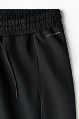 Pantalón de jogging deportivo de corte holgado, confeccionado en tejido técnico con tecnología de absorción de humedad. Presenta cintura elástica con cordón de ajuste, bolsillos laterales, ribetes verticales en las piernas y cordón elástico ajustable en los bajos.