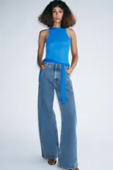 Jeans de tiro alto con corte wide leg y largo completo. Presenta diseño de cinco bolsillos, trabillas en la cintura y cierre frontal con cremallera y botón, con un acabado de efecto lavado.