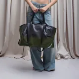 Bolso tote grande de cuero sintético negro con doble asa de mano y correa larga al hombro.