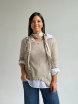 Sweater de punto fino en color beige, con cuello redondo y mangas tres cuartos. El diseño incluye una bufanda integrada del mismo tejido con detalles de puntilla en los extremos.