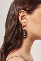 Aro tipo argolla pequeña dorada con dije colgante en forma de cuerno de resina negra, decorado con incrustaciones de strass.