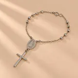 Pulsera tipo denario de plata 925, compuesta por una cadena de eslabones intercalados con cuentas esféricas facetadas, medalla ovalada con relieve y dije colgante en forma de cruz.