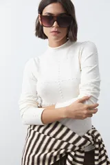 Polera de tejido de punto color celeste, con cuello alto y textura de pequeños puntos en relieve formando una cuadrícula en el frente y las mangas. De corte ajustado y manga larga.