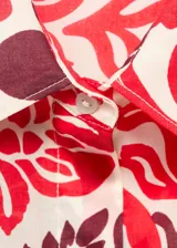 Camisa de corte recto y diseño holgado, confeccionada en algodón con estampado floral en tonos rojos y bordó sobre fondo crudo. Presenta cuello camisero clásico, cierre frontal con botones y mangas largas.