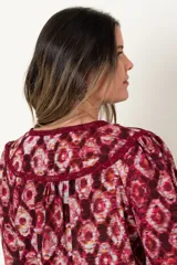 Blusa estampada color borgoña con diseño de rombos, de manga larga y escote en V con aplique de galón.