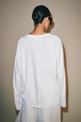 Camiseta blanca de manga larga con cuello redondo y cierre frontal de botones, corte regular y bajo recto.