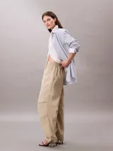 Pantalón parachute Calvin Klein de nailon suave con diseño holgado (loose fit), cintura elástica con cordón interior y cierre de botón y cremallera. Presenta bolsillos superpuestos y puños ajustables con cordón y cremallera.
