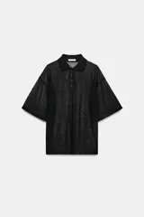 Polo negro confeccionado en hilatura con mezcla de viscosa, de textura rústica y ligera transparencia, con cuello solapa, cierre frontal de botones y manga corta de corte holgado.