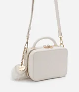 Bolso transversal tipo camera bag, color blanco con textura matelasse de rombos. Tiene correa fina ajustable y removible, cierre de cremallera y colgante de pompón.