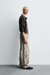 Pantalón de corte relajado confeccionado en algodón, con diseño de efecto lavado y estampado abstracto en tonos grises y beige. Presenta cinco bolsillos y cierre frontal con cremallera y botón.